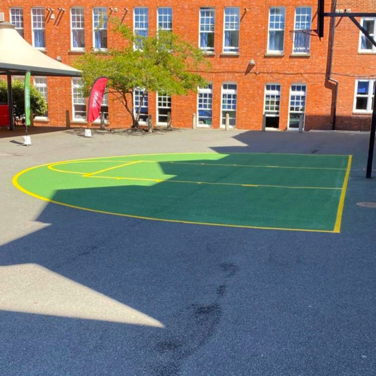 Green basketball court with one hooppainted onto a tarmac courtyard.